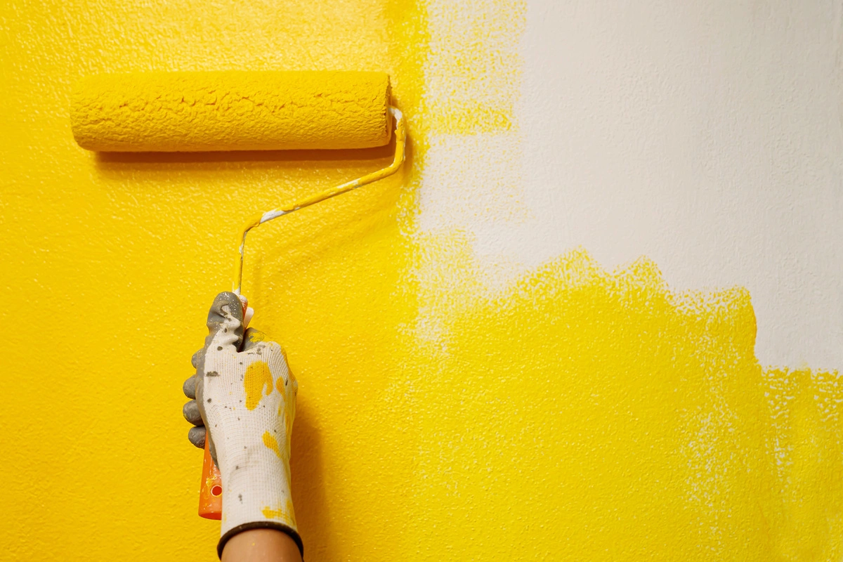 Personne appliquant de la peinture jaune sur un mur à l'aide d'un rouleau, illustrant un service professionnel de peinture en cours.